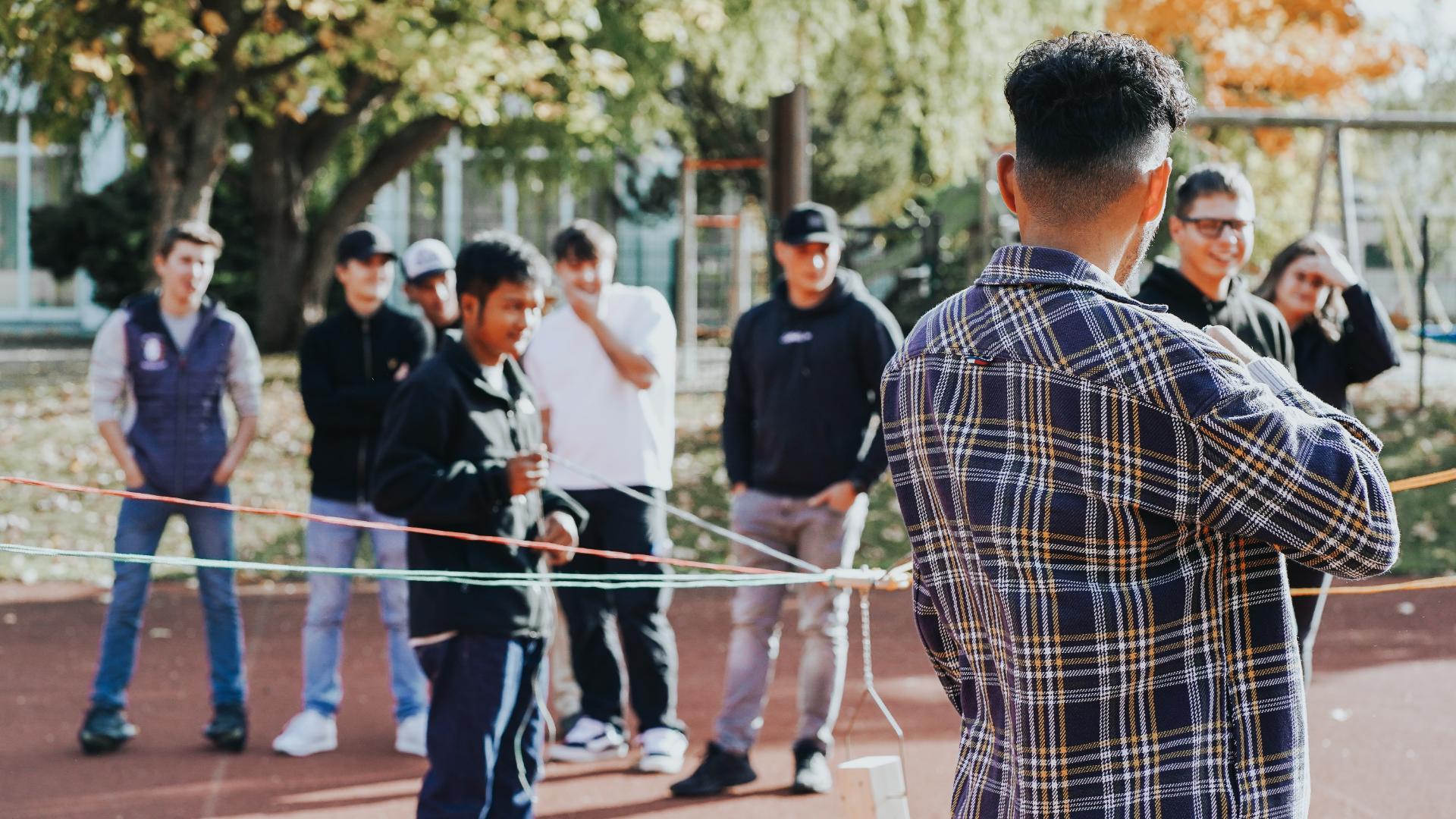 Eine Gruppe junger Männer steht im Kreis um ein Geschicklichkeitsspiel zu lösen.