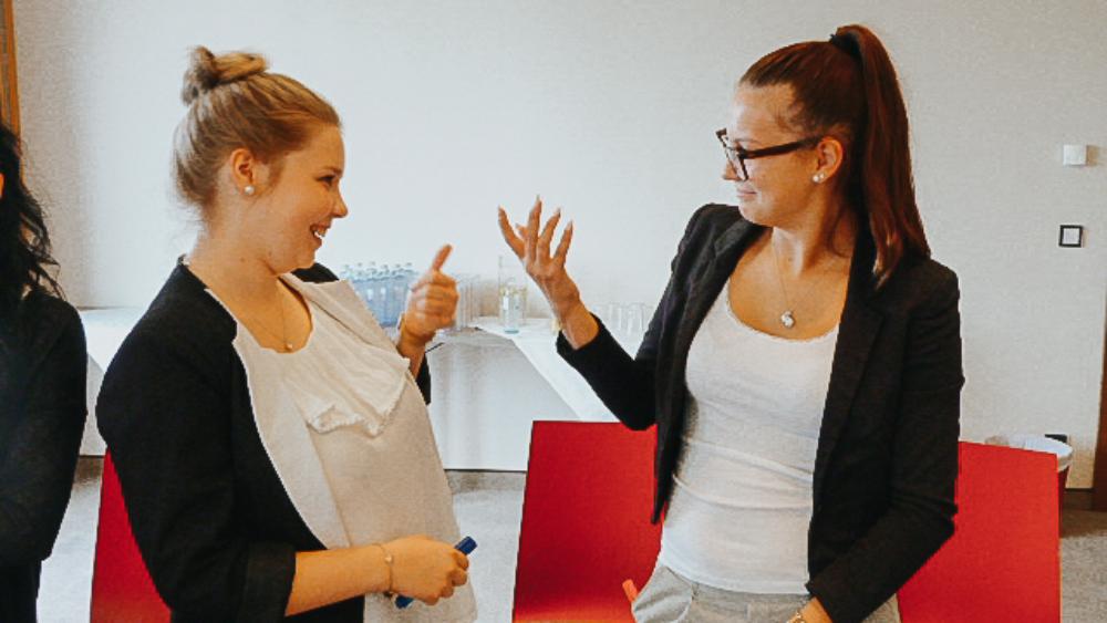Zwei junge Frauen in Business Kleidung unterhalten sich miteinander.