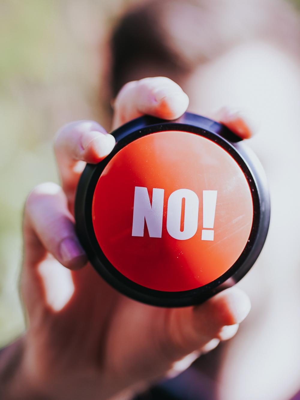 Eine Person hält einen roten Button mit der Aufschrift "No" in die Kamera.